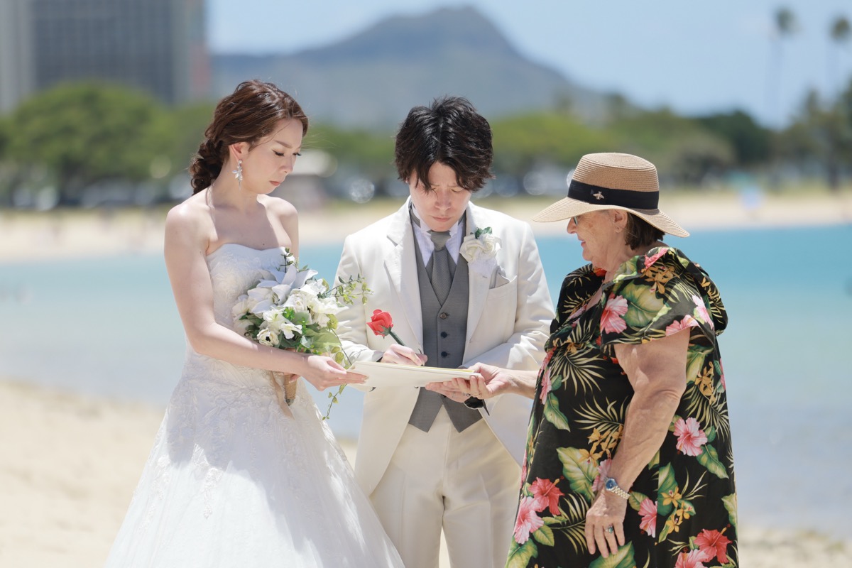 ダイヤモンドヘッドを望むビーチで結婚証明書にサインする新郎新婦