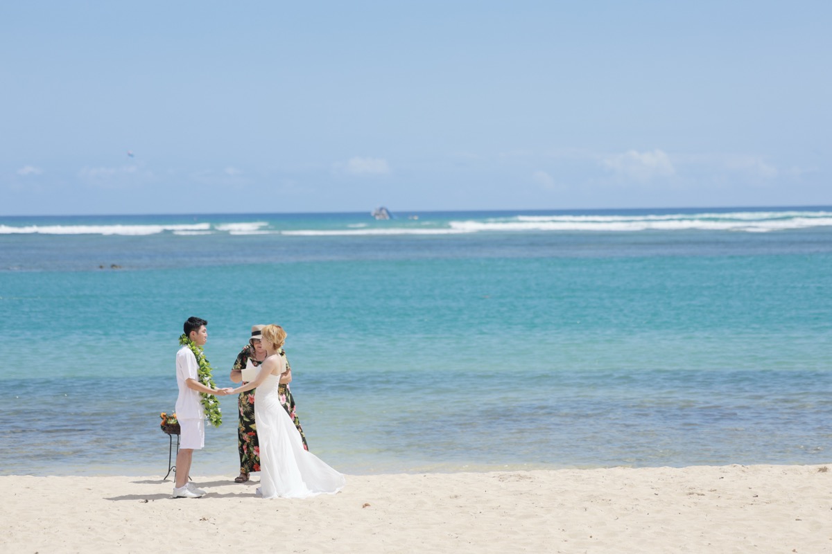 アラモアナビーチで青い海を背景に挙式する新郎新婦