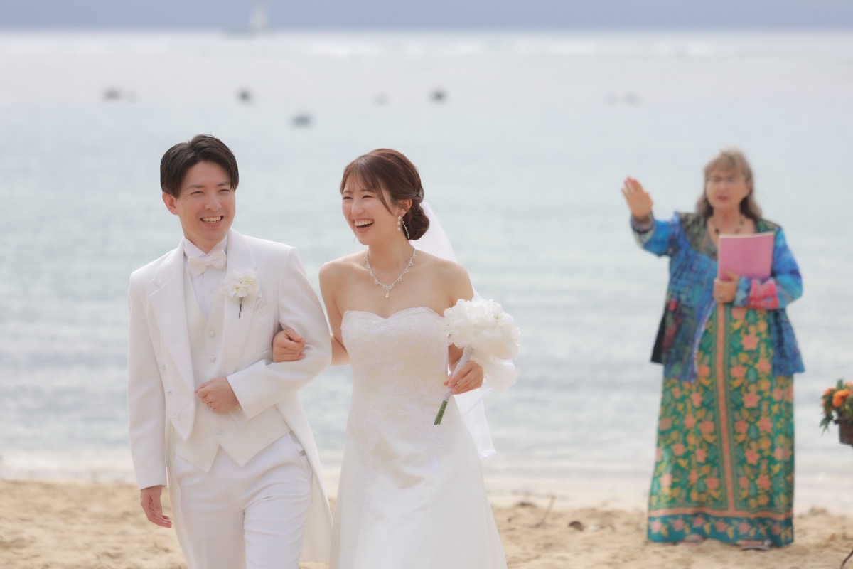 ビーチウェディングで笑顔で歩く新郎新婦