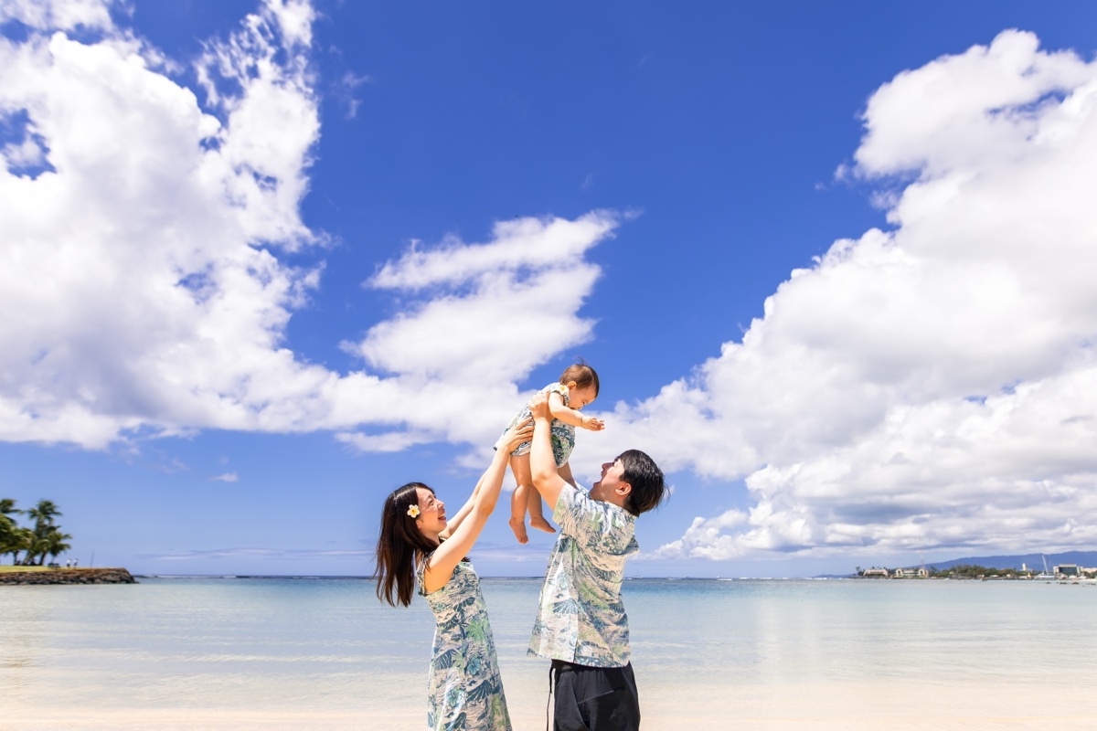ビーチで子どもを高く抱き上げる夫婦