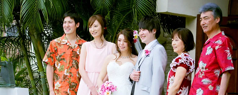 ハワイの会場前でアロハシャツの家族に囲まれた新郎新婦のウェディング記念写真