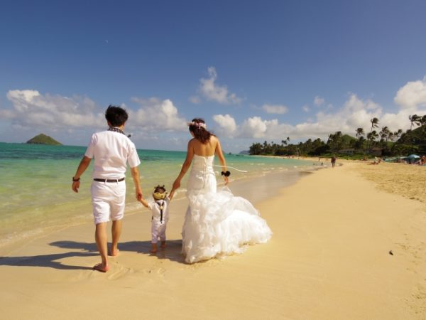 美しい砂浜を子供の手を引いて歩く夫婦のブライダルフォト