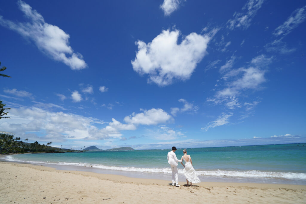 ハワイの海岸線の長いビーチでウェディングドレスを着て撮影する花嫁