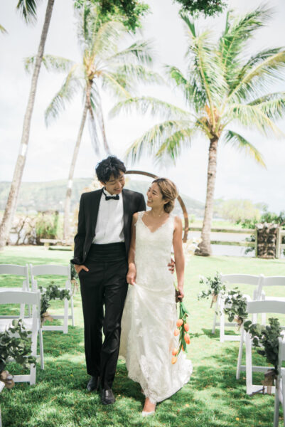 マウロアガーデンのバージンロードを笑顔で歩く新郎新婦｜ヤシの木に囲まれたハワイのガーデンウェディングフォト